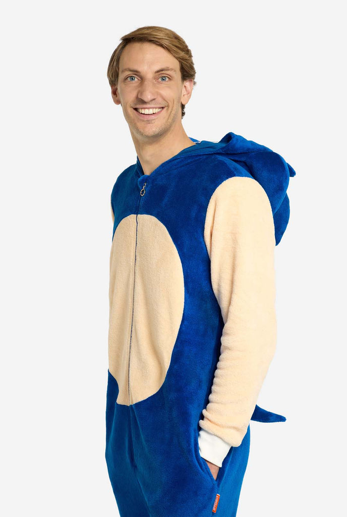 A man is wearing a playful blue and beige Sonic the Hedgehog-themed adult onesie from OppoSuits. The cozy onesie features a zip-up front and an attached hood designed to resemble Sonic’s iconic face, complete with ears and an expressive gaze. The blue body of the suit contrasts with a beige belly, mimicking Sonic's classic look. Standing side ways and looking in the camera.