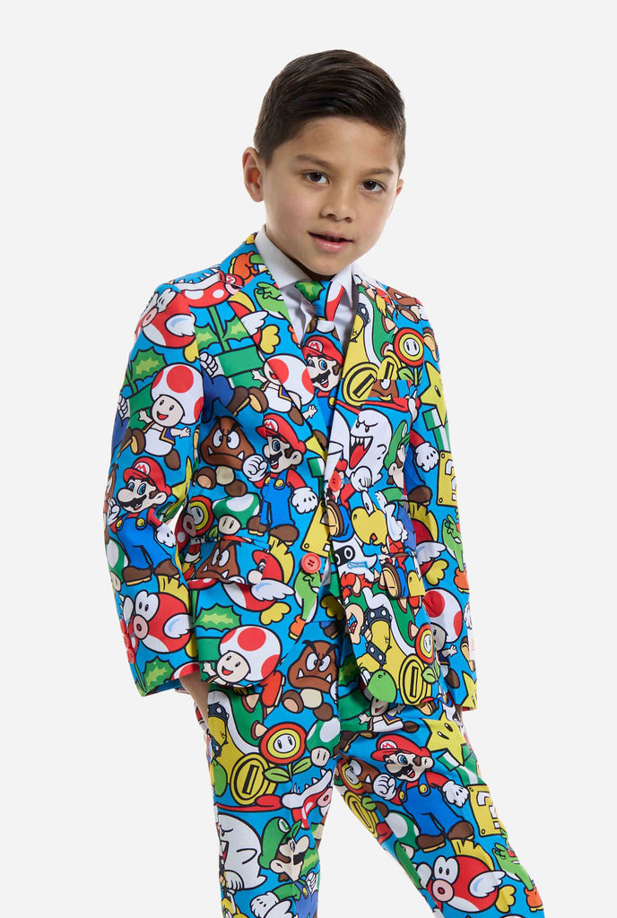 Image of kid wearing a Super Mario all over print suit, consisting of blazer, pants and tie. Main color is blue, but there is also yellow, red and white.