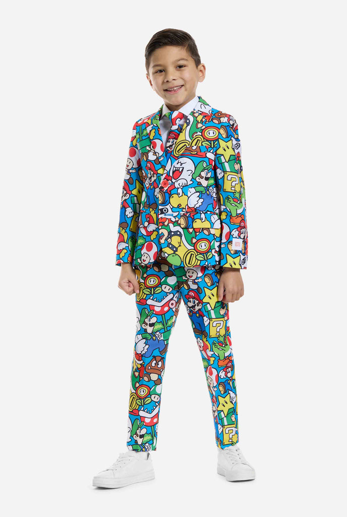 Image of kid wearing a Super Mario all over print suit, consisting of blazer, pants and tie. Main color is blue, but there is also yellow, red and white.