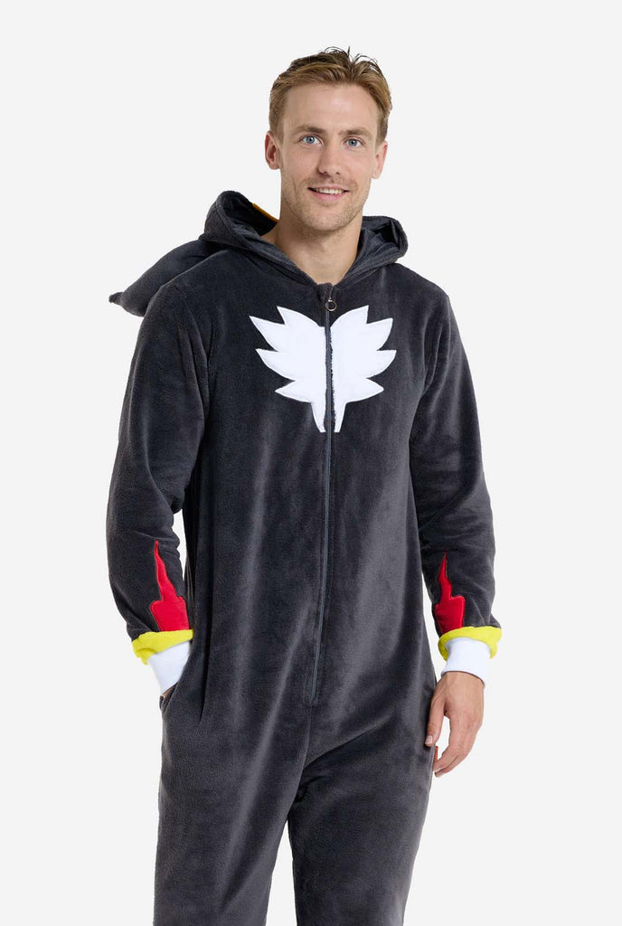 A man wearing a plush black onesie inspired by the popular hedgehog character Shadow, featuring spiky red and black accents on the hood, a white chest emblem, and yellow wrist details. The onesie is made from soft fleece material, offering comfort and a playful design for cosplay, lounging, or themed events. The person smiles while the hood is lying on his back. Perfect for fans of gaming or animated characters.