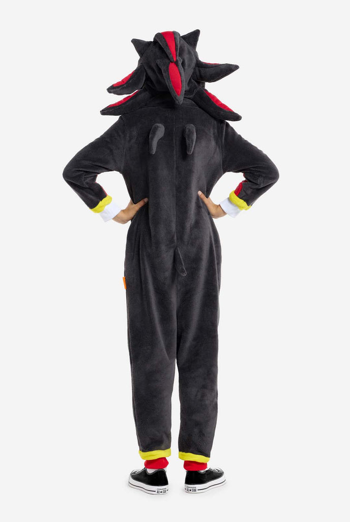 A kid wearing a plush black kids onesie inspired by the popular hedgehog character Shadow, featuring spiky red and black accents on the hood, a white chest emblem, and yellow wrist details. The onesie is made from soft fleece material, offering comfort and a playful design for cosplay, lounging, or themed events. View from the back. Perfect for fans of gaming or animated characters.