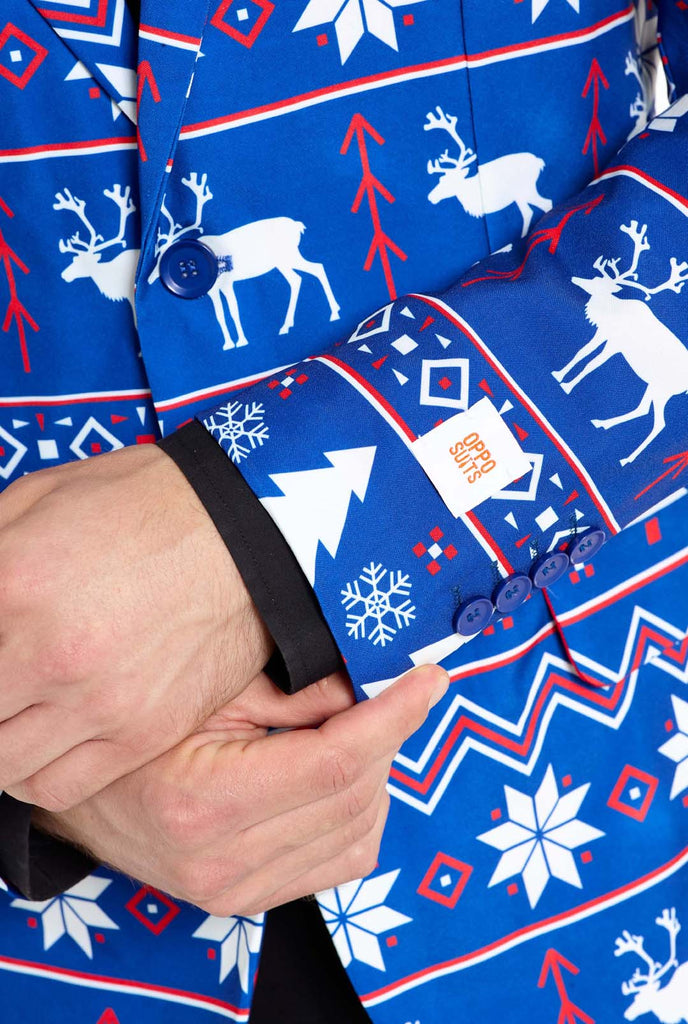 Man wearing blue Christmas blazer for men with Nordic Christmas figures. Man also wearing a black pants and black men's shirt. Sleeve close up.