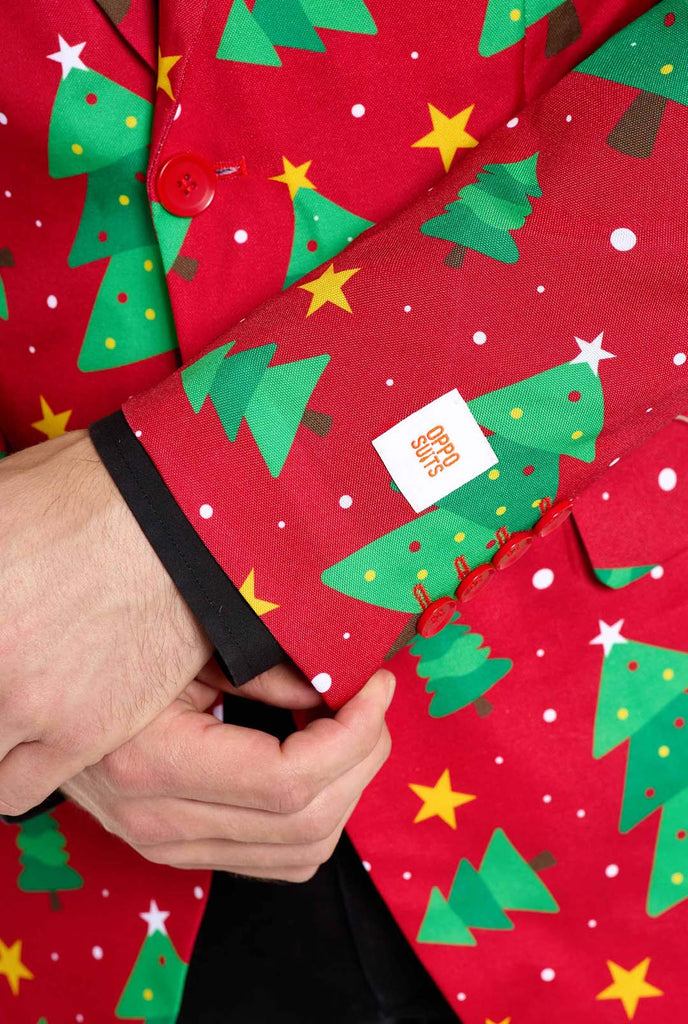 Man wearing red Christmas blazer for men with Christmas trees and stars print. Man also wearing a black pants and black men's shirt. Sleeve close up.