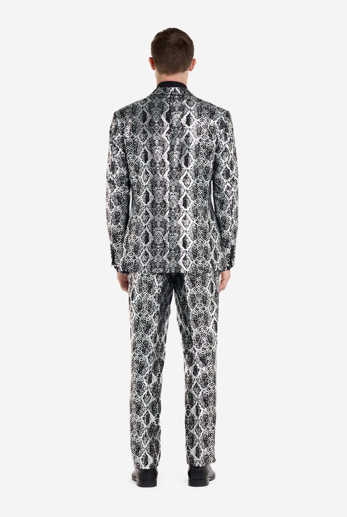 A man is wearing an eye-catching silver and black snake-print suit by OppoSuits. The striking suit features a bold snakeskin pattern, offering a sleek, fashionable look perfect for parties, events, or making a daring fashion statement. The men suit is paired with a black dress shirt and a matching snake-print tie, adding a sophisticated edge to the overall ensemble. View from the back.