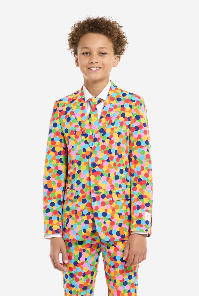 In this image, a kid is wearing a colorful, polka-dotted suit. The suit has a bright pattern with circles in various colors including orange, yellow, pink, green, blue, and red, arranged in a confetti-like style.