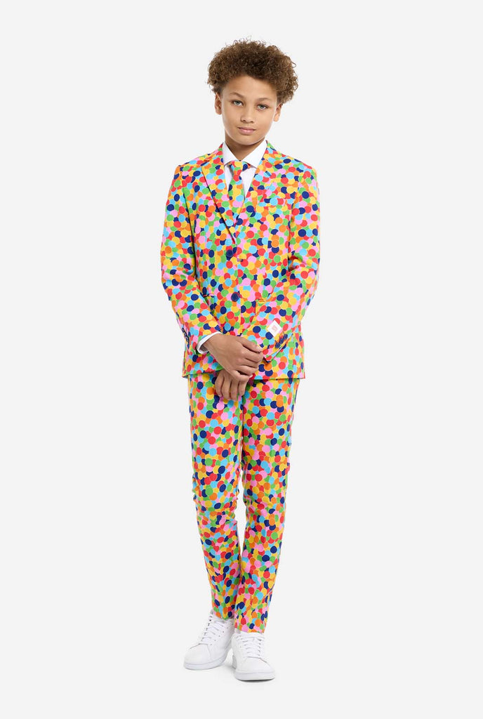 In this image, a kid is wearing a colorful, polka-dotted suit. The suit has a bright pattern with circles in various colors including orange, yellow, pink, green, blue, and red, arranged in a confetti-like style.