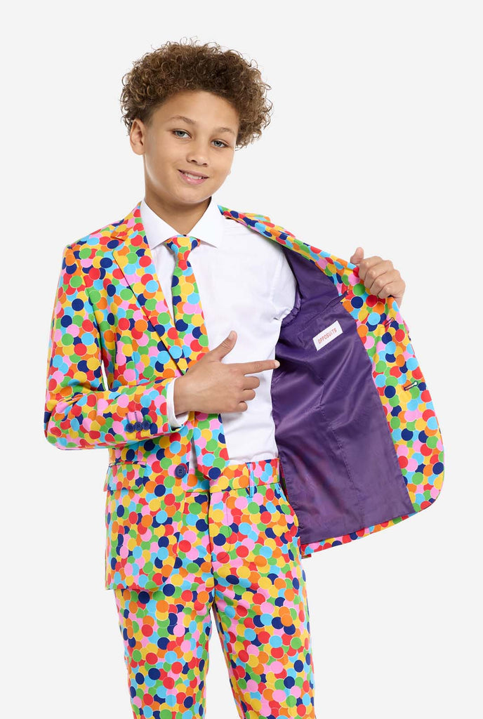 In this image, a kid is wearing a colorful, polka-dotted suit. The suit has a bright pattern with circles in various colors including orange, yellow, pink, green, blue, and red, arranged in a confetti-like style.