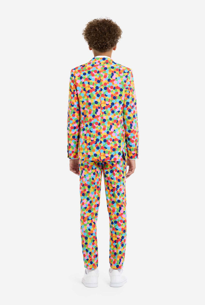 In this image, a kid is wearing a colorful, polka-dotted suit. The suit has a bright pattern with circles in various colors including orange, yellow, pink, green, blue, and red, arranged in a confetti-like style.