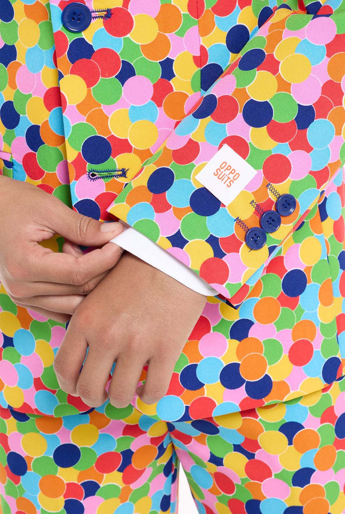 In this image, a kid is wearing a colorful, polka-dotted suit. The suit has a bright pattern with circles in various colors including orange, yellow, pink, green, blue, and red, arranged in a confetti-like style.