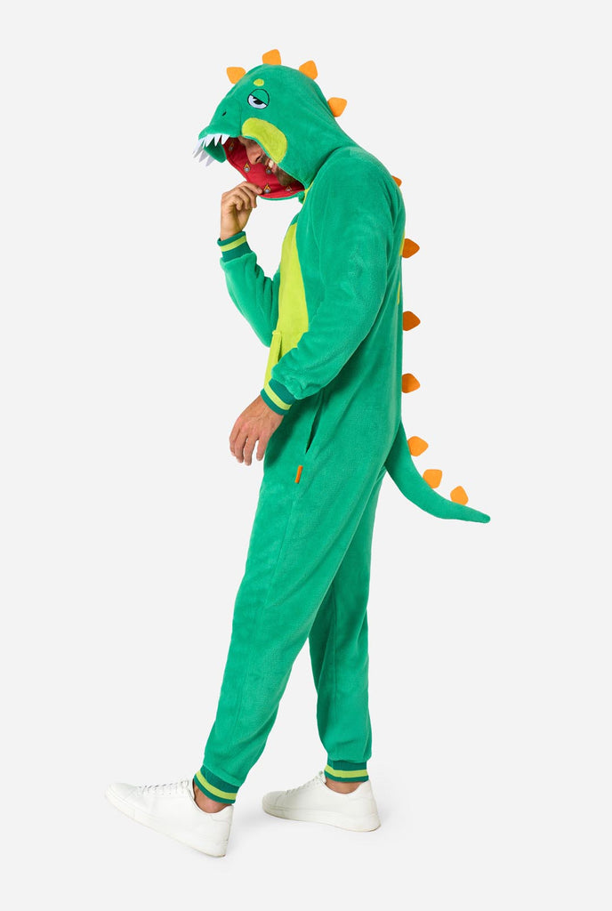 A man is wearing a green dinosaur adult onesie featuring playful hood details and cozy, soft material, perfect for lounging or costume events. He is standing sideways and holding the hood over his head. Full body image.