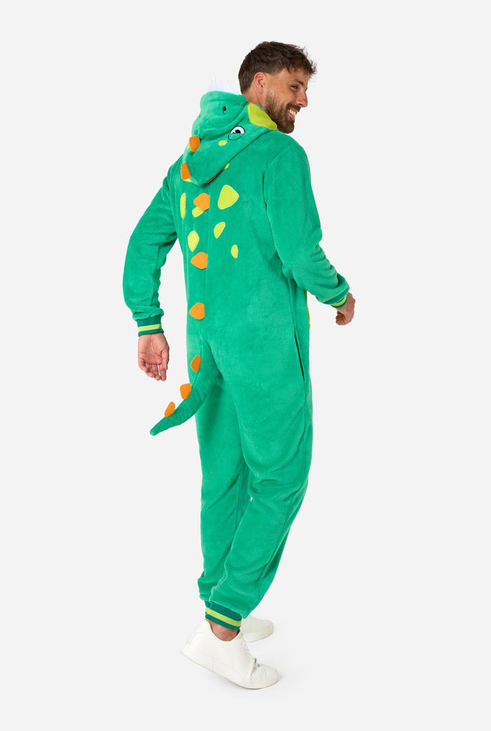 A man is wearing a green dinosaur adult onesie featuring playful hood details and cozy, soft material, perfect for lounging or costume events. He is standing sideways and showing the back of the onesie.