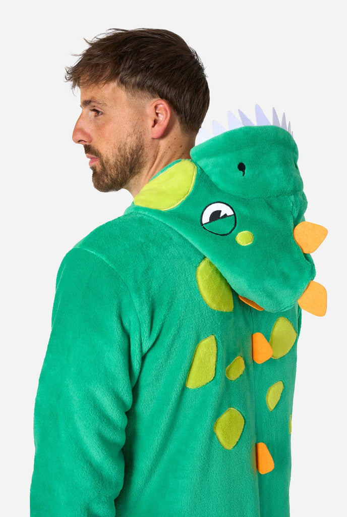 A man is wearing a green dinosaur adult onesie featuring playful hood details and cozy, soft material, perfect for lounging or costume events. He is standing sideways and holding the hood over his head. Close up of the upper part of his body