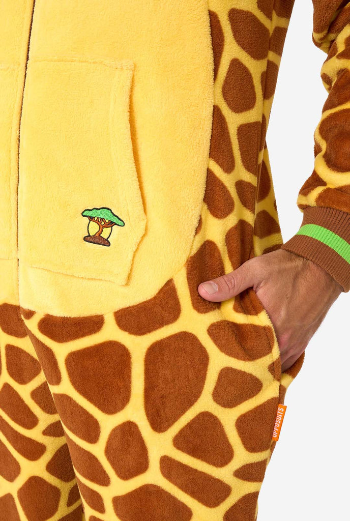 A smiling man is wearing a brown and yellow adult onesie designed as a giraffe. The onesie features a hood resembling a Giraffes head, and giraffe details, perfect for cozy lounging or costume parties. Pocket close-up.