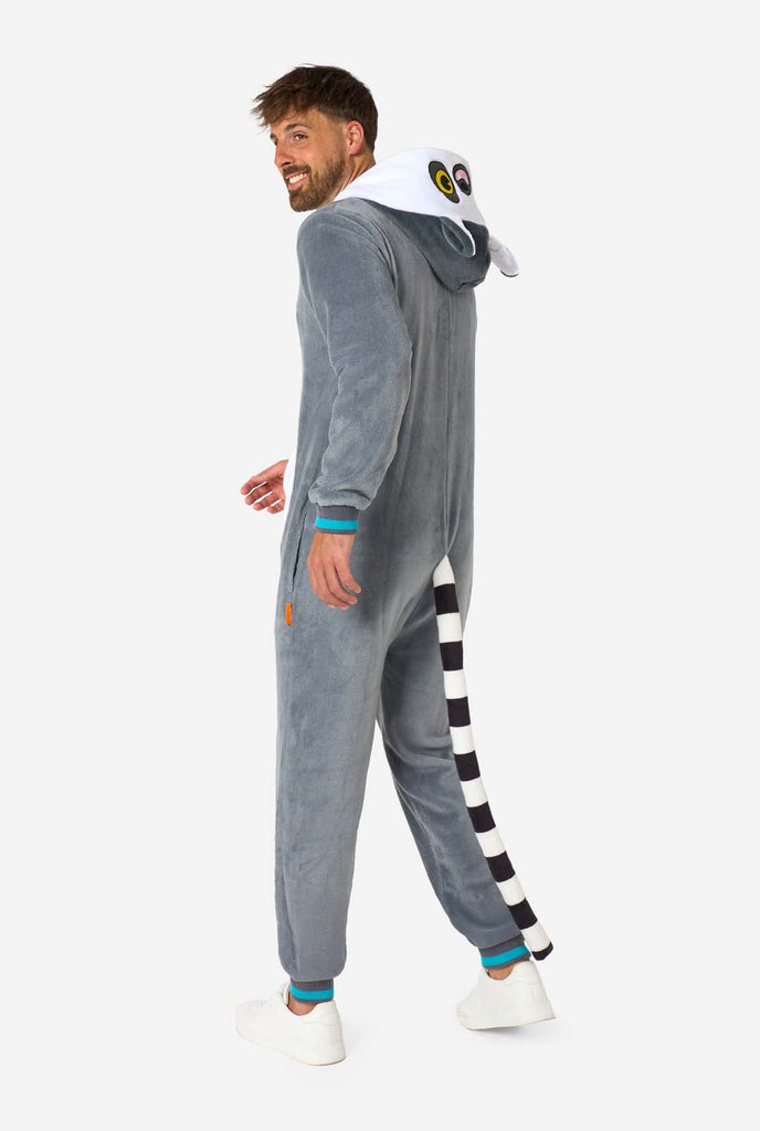 A man is wearing a grey and white lemur adult onesie featuring playful hood details and cozy, soft material, perfect for lounging or costume events. Including black and white tail. Full body image from the side.