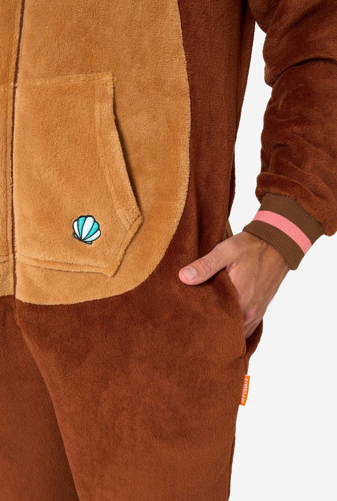 A smiling man is wearing a brown adult onesie designed as an otter. The onesie features a hood with ears, a cute face, and playful otter details, perfect for cozy lounging or costume parties. Pocket close up.