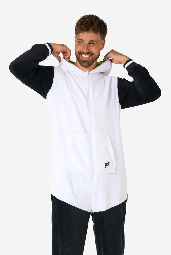 A smiling man wearing a panda-themed adult onesie. This cozy onesie features black and white panda colors with a playful hood showcasing panda ears and a cute face. Perfect for lounging or fun costume occasions. The hood is flat on his back.