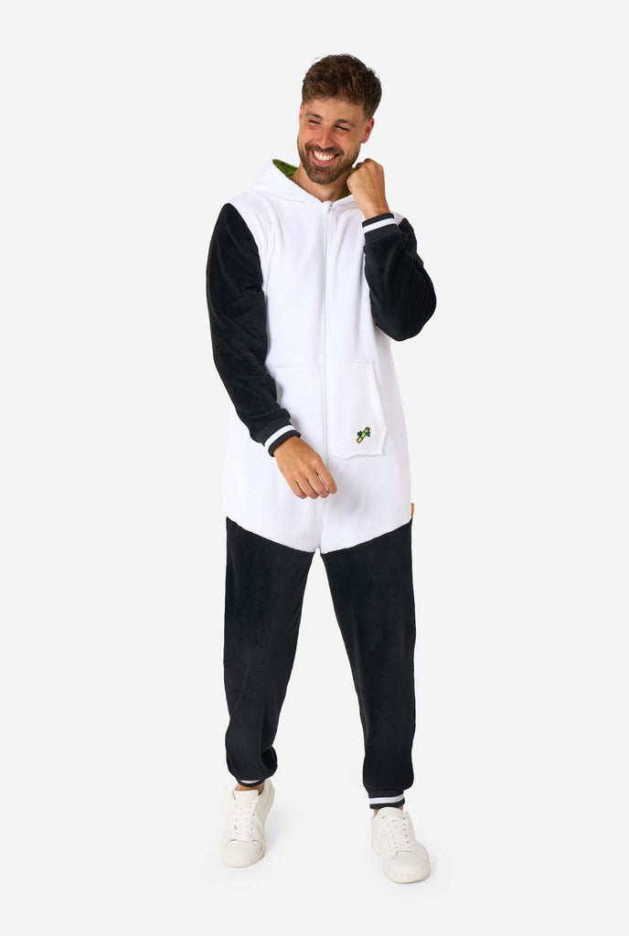 A smiling man wearing a panda-themed adult onesie. This cozy onesie features black and white panda colors with a playful hood showcasing panda ears and a cute face. Perfect for lounging or fun costume occasions. Full body image with the hood on his back.