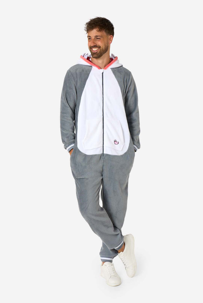 A man is wearing a grey and white shark adult onesie featuring playful hood details and cozy, soft material, perfect for lounging or costume events. Full body image and two hands in the pockets.