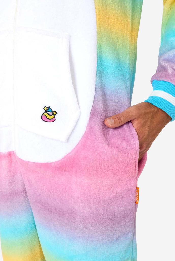 A man wearing a colorful adult onesie designed as a rainbow unicorn. The onesie features a vibrant gradient of pastel colors, a golden horn, and playful unicorn details. Close-up image pocket.