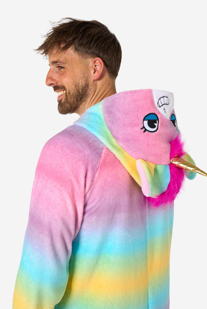 A man wearing a colorful adult onesie designed as a rainbow unicorn. The onesie features a vibrant gradient of pastel colors, a golden horn, and playful unicorn details, perfect for cozy lounging or costume parties. The hood is lying flat on his back. Close-up image upper body side view.