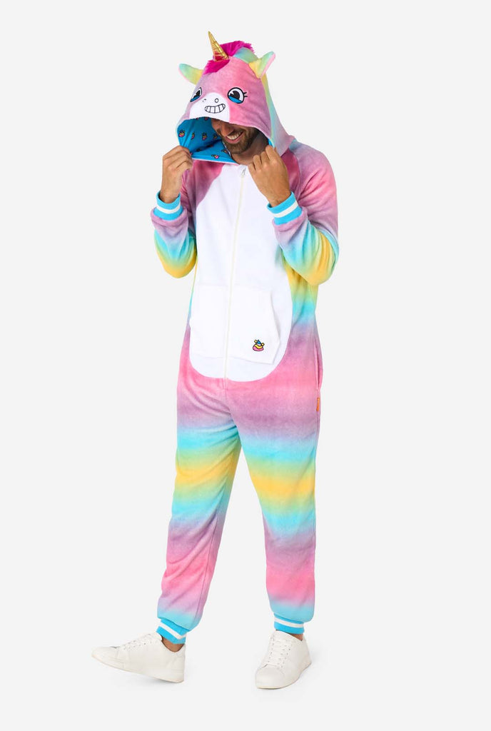 A man wearing a colorful adult onesie designed as a rainbow unicorn. The onesie features a vibrant gradient of pastel colors, a golden horn, and playful unicorn details, perfect for cozy lounging or costume parties. Full body image and man is looking at the floor.