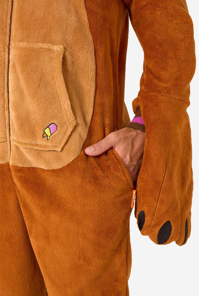 A cheerful man wearing a brown adult onesie designed as a walrus. The onesie features a hood with fangs, stitched gloves resembling paws, and playful walrus details, perfect for cozy lounging or costume parties. Pocket close up.