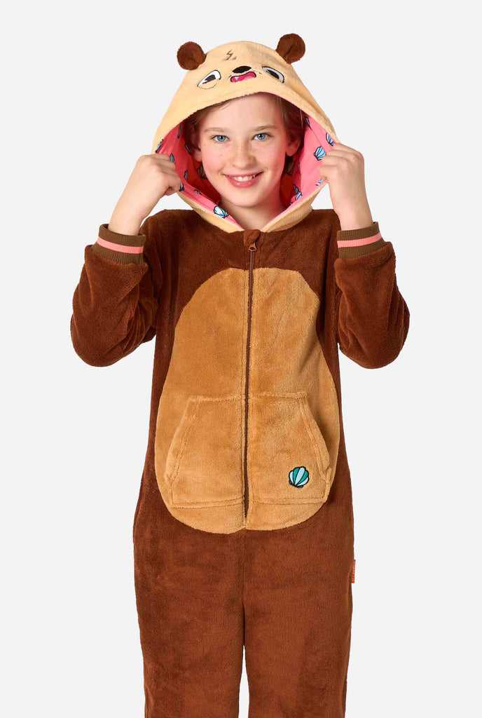 A smiling kid is wearing a brown kids onesie designed as an otter. The onesie features a hood with ears, a cute face, and playful otter details.