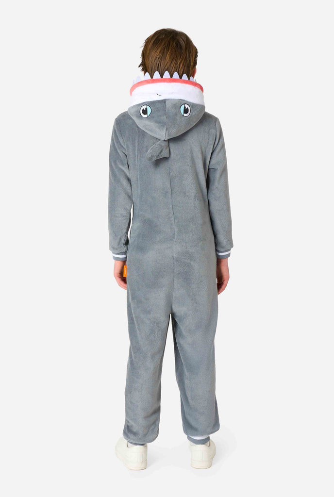 A kid is wearing a grey and white shark kids onesie featuring playful hood details and cozy, soft material, perfect for lounging or costume events. View from the back.