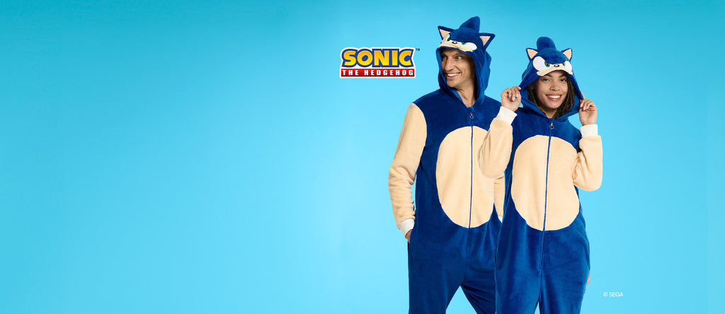 Man and woman wearing Sonic the Hedgehog themed onesie. Blue and beige, with the Head of Sonic on the hood. Image has a Sonic logo and a light blue background.