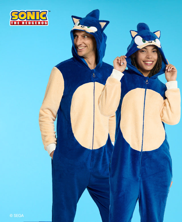 Man and woman wearing Sonic the Hedgehog themed onesie. Blue and beige, with the Head of Sonic on the hood. Image has a Sonic logo and a light blue background.